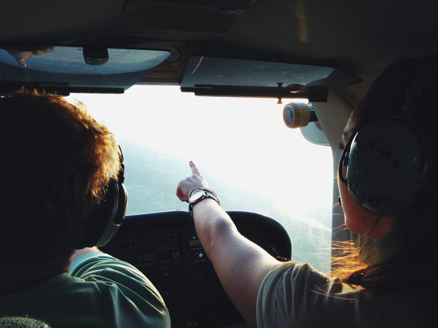 Two people in a small aircraft cockpit, navigating with headsets during a daytime flight.